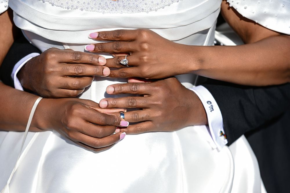 Close-up of newlywed couple's hands showing wedding rings, bride in white dress, groom in white shirt.