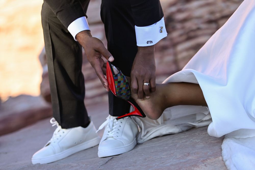 Bride and groom in wedding attire wearing white sneakers, with red-soled shoes visible during outdoor ceremony.