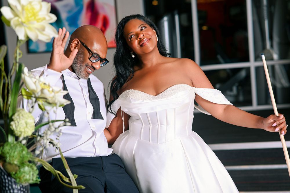 A bride in an off-shoulder white gown and groom in suit sit together at an elegant wedding celebration.