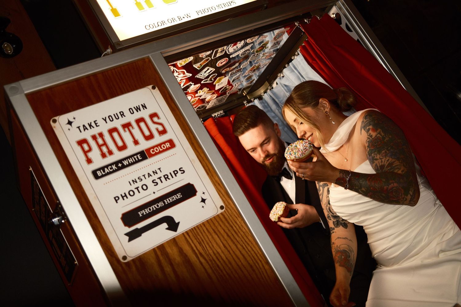 Retro photo booth with checkered floor, heart wallpaper, orange curtain, stool, and color or B&W photo strips sign.