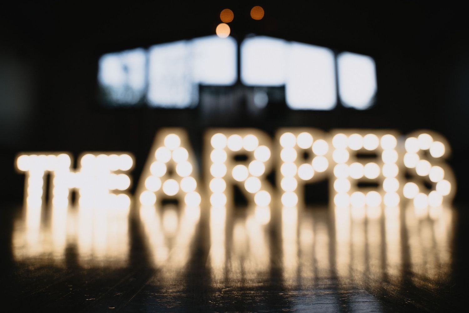 Black and white wedding photo with illuminated ARPEIS marquee letters on dance floor as couple dances nearby.