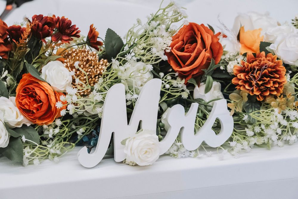 White Mrs. sign surrounded by elegant fall wedding floral arrangement with burnt orange, rust, and ivory roses.