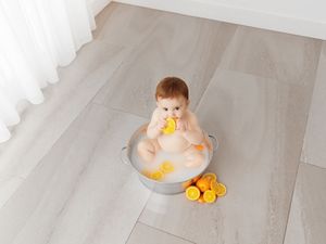 Baby sitting in a metal tub with milk and orange slices, chewing on a fresh orange slice on a light wood floor.