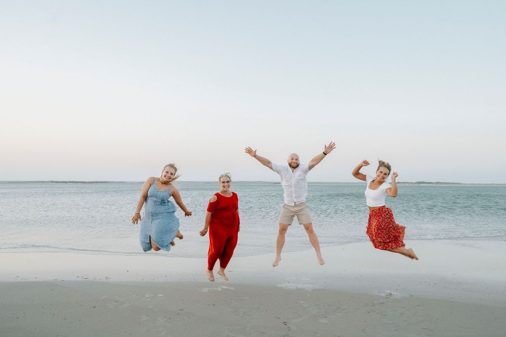 Four joyful people jumping on a sandy beach at sunset with calm ocean waters in the background.