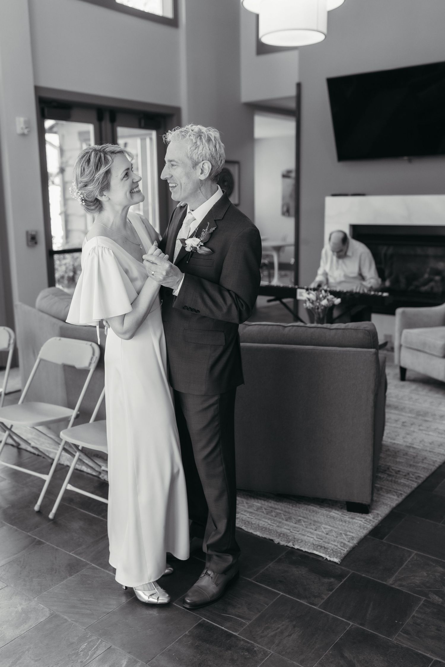 Black and white photo of a couple sharing a first dance in elegant wedding attire inside a modern venue.
