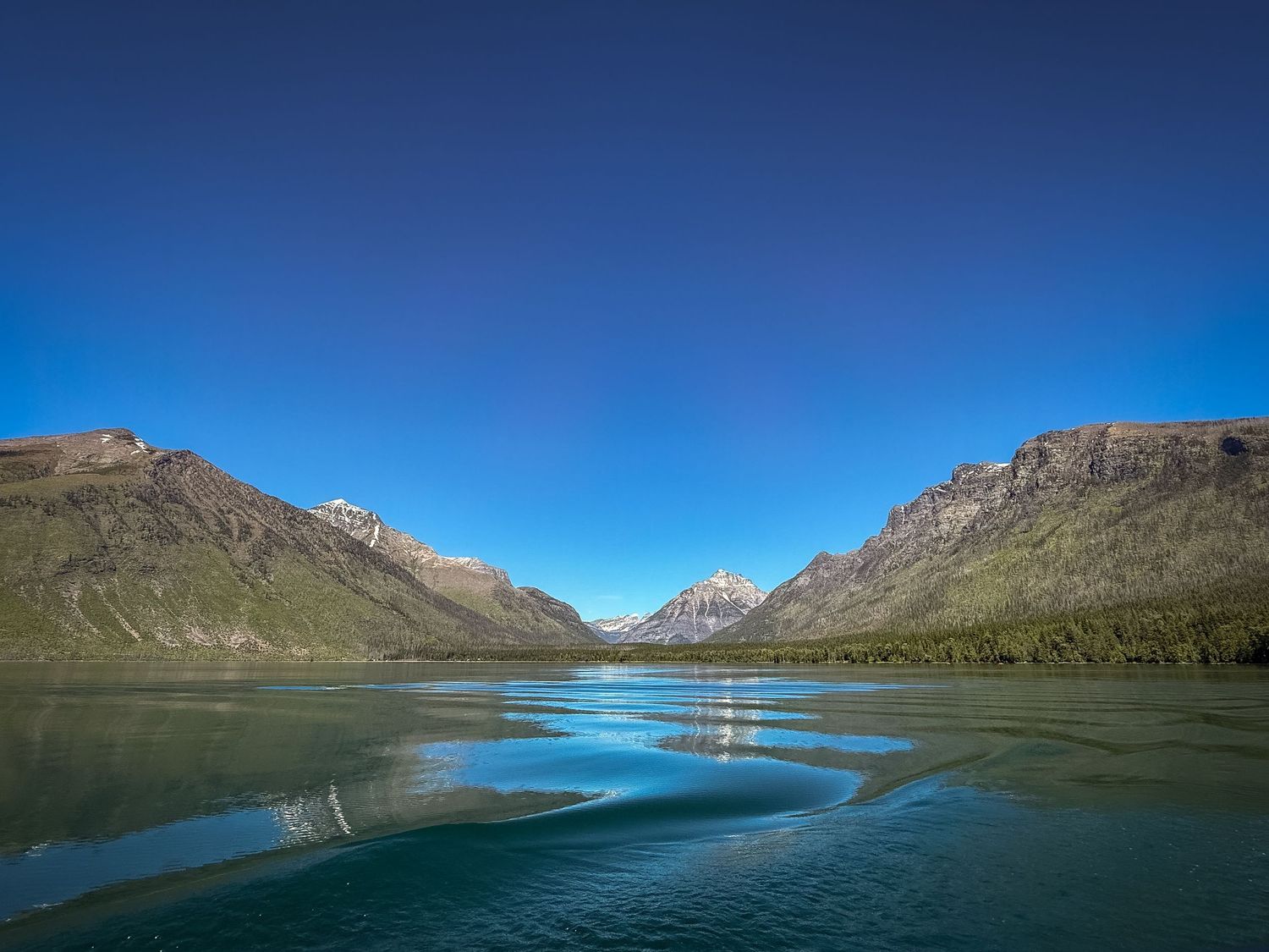 Serene glacial lake reflecting snow-capped mountains under a clear blue sky in a pristine wilderness valley.