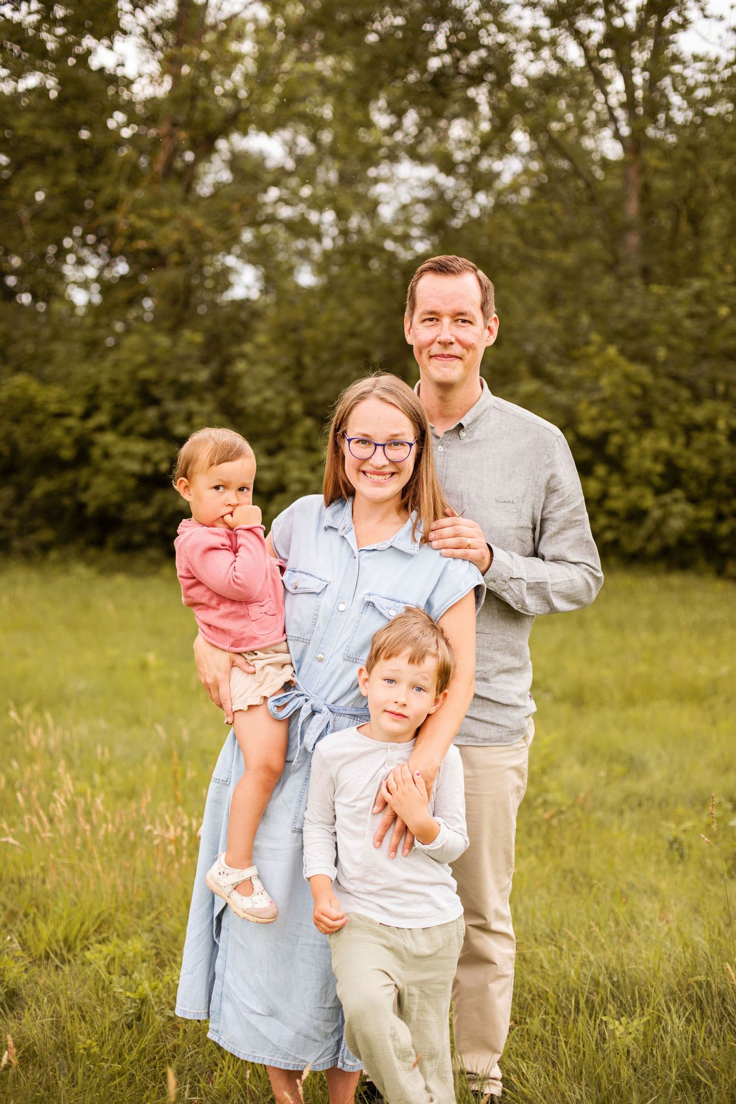A sweet moment captured in a sunny meadow with tall grass showing a small child in a white dress in the foreground.