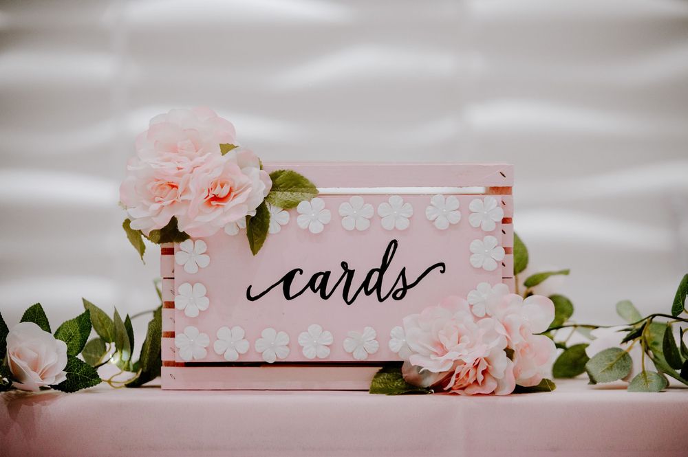 Pink floral wedding card box decorated with roses and daisy pattern on a pink tablecloth.