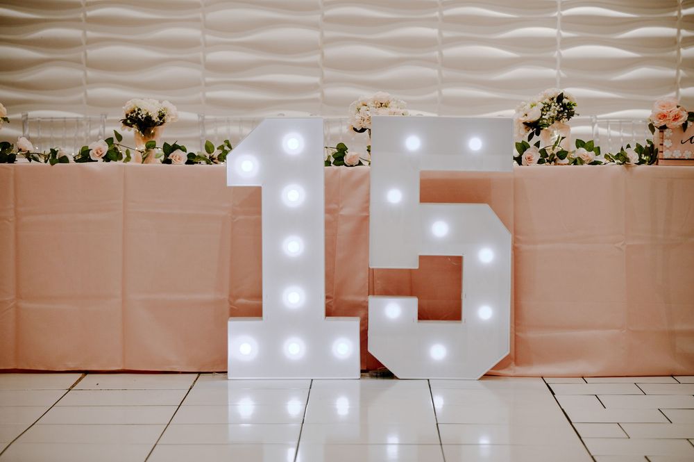 Large illuminated marquee number 15 with white light bulbs displayed at a quinceañera celebration.