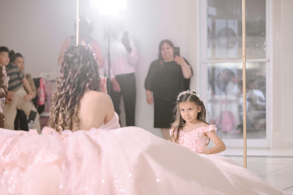 Young girl in pink dress looks up at woman in large pink gown at elegant quinceañera celebration.
