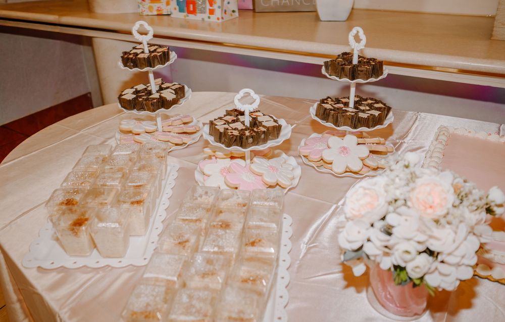 Elegant quinceañera dessert table with tiered cake stands, cookies, and white rose floral arrangement.