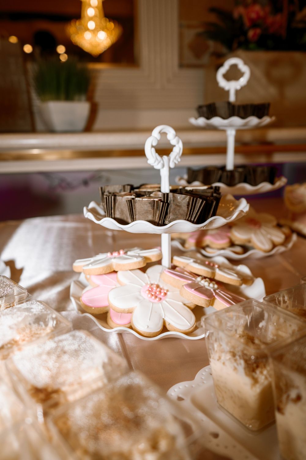 Tiered white dessert stand with decorated cookies and chocolates at quinceañera celebration.
