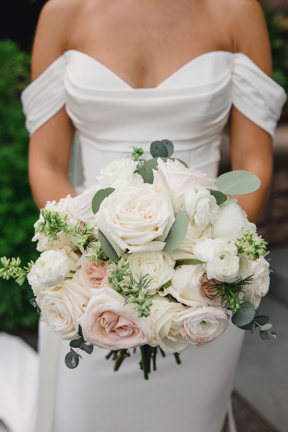 Bride in off-shoulder white gown holding elegant bouquet of blush and white roses with eucalyptus greenery. OceanCliff Newport RI Wedding