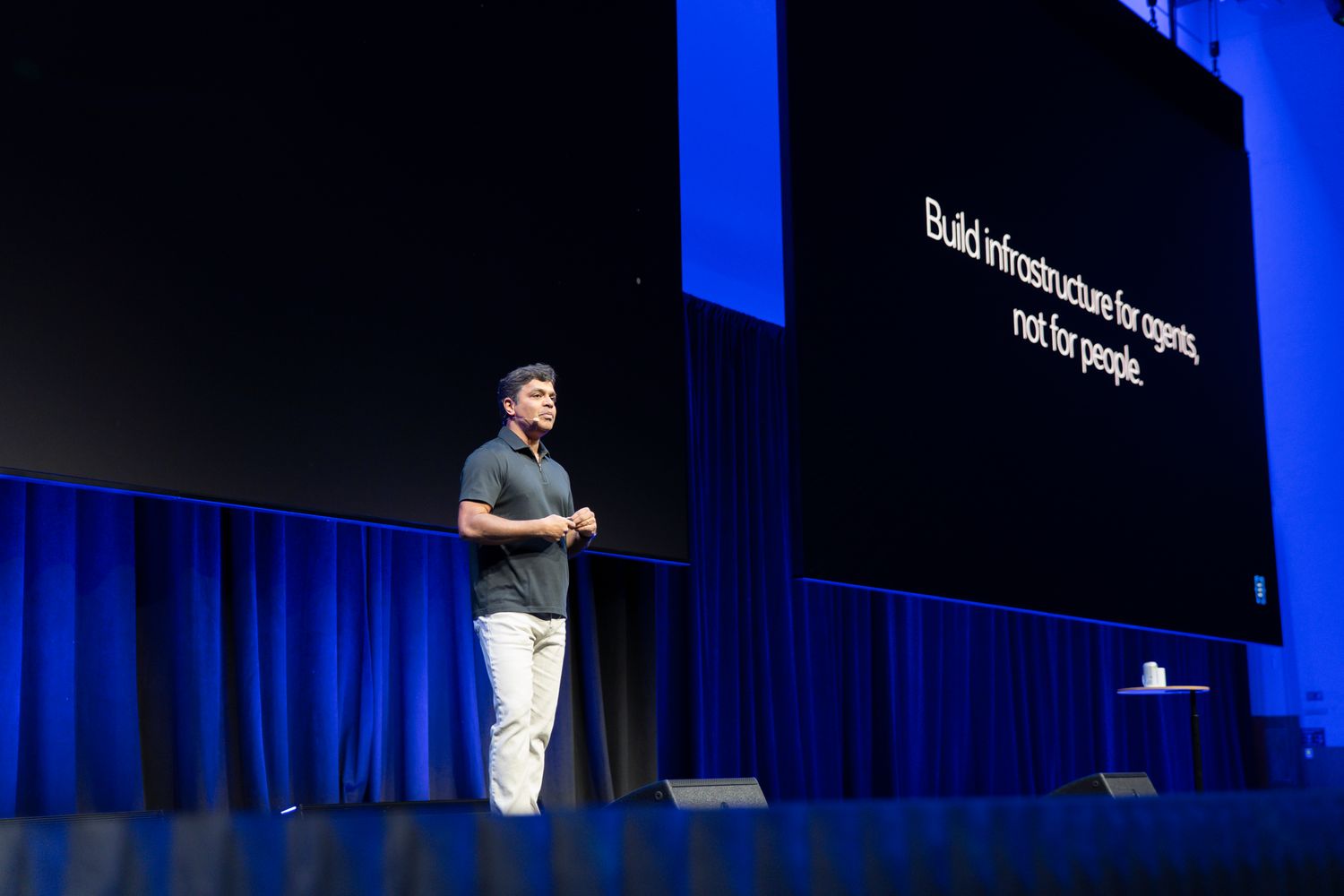 Speaker presenting on stage at tech conference with slide reading Build infrastructure for agents, not for people.
