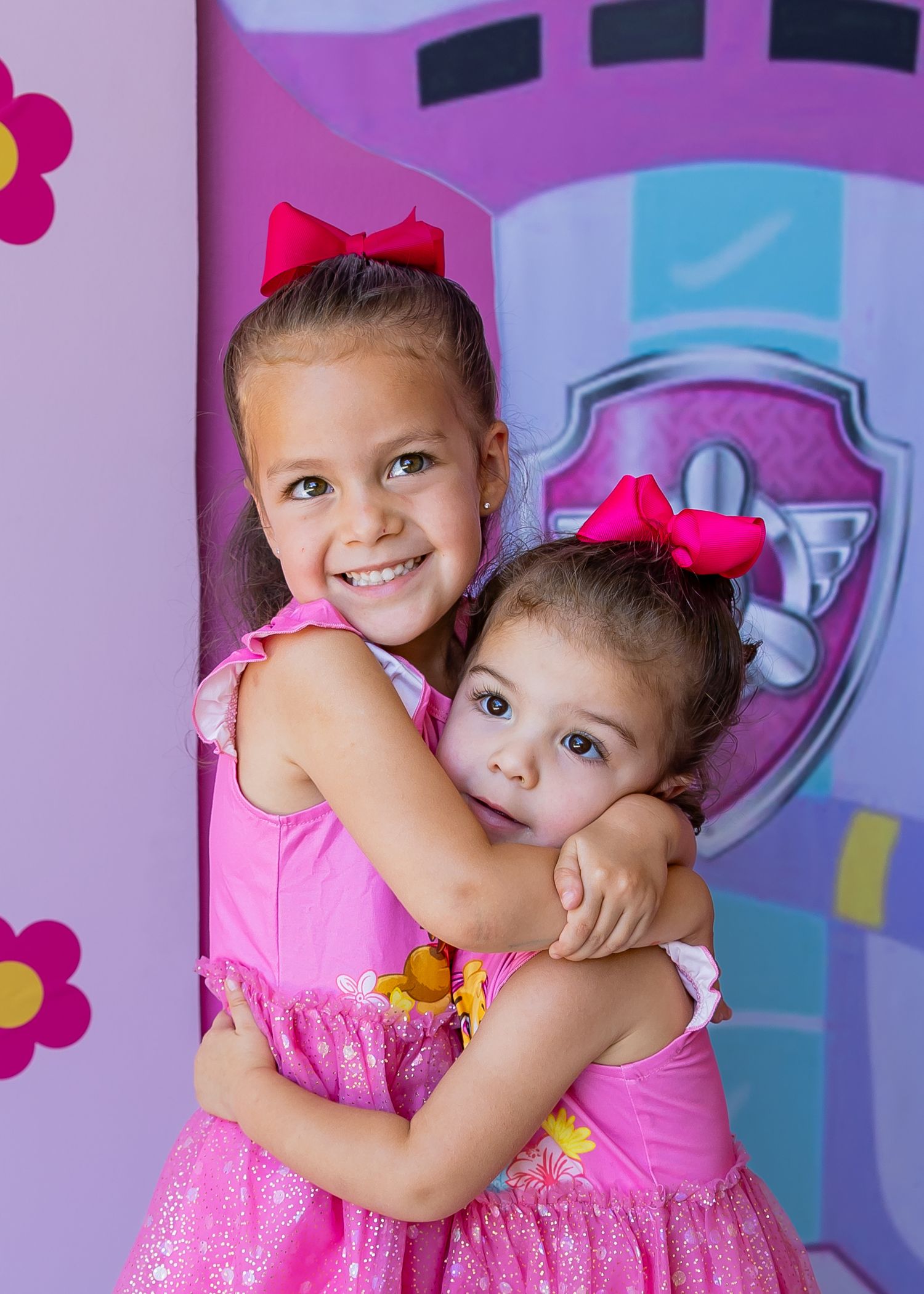 A mother holds and kisses her young daughter at a Paw Patrol themed 4th birthday party with balloon decorations.