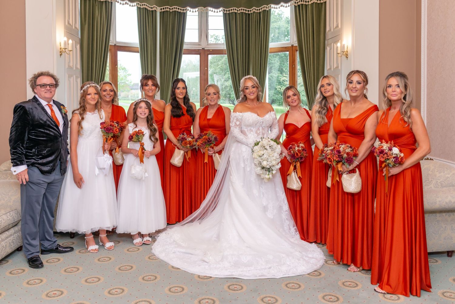 Bride in white gown poses with bridesmaids in orange dresses and flower girl in elegant venue wedding photo at Runcorn Town Hall