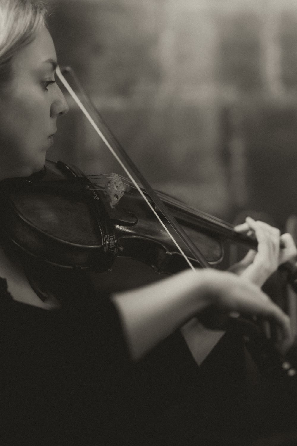 Black and white photo of a woman playing violin, captured in a moody, artistic side profile shot.
