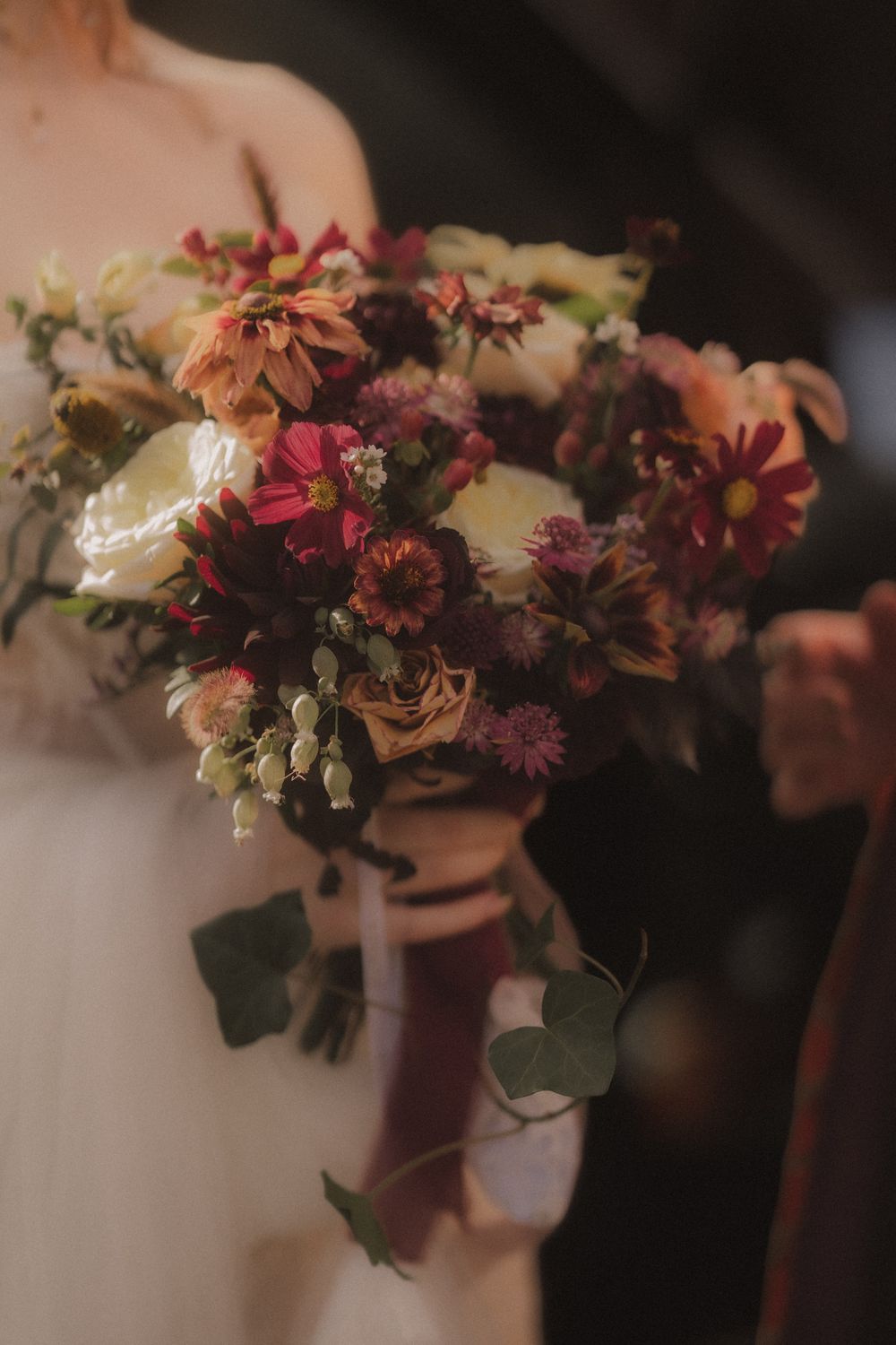 Bride holding a lush autumn bridal bouquet with deep red, pink, and cream flowers with eucalyptus and ribbon.