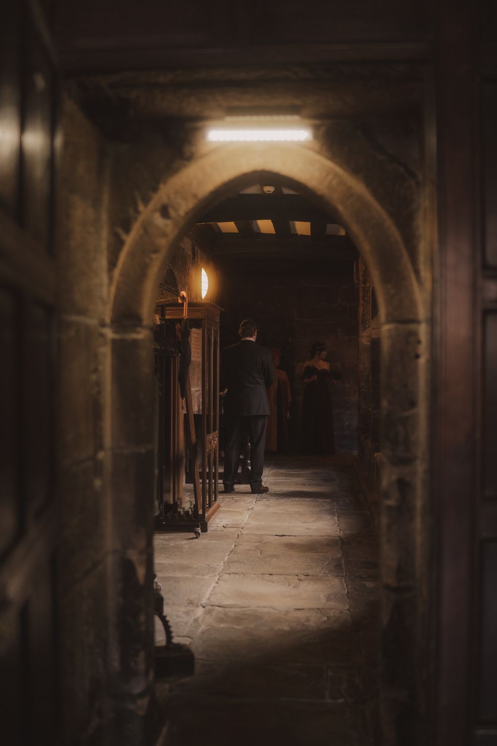 Person walking through a dimly lit stone archway corridor in an ancient building with warm torch lighting.