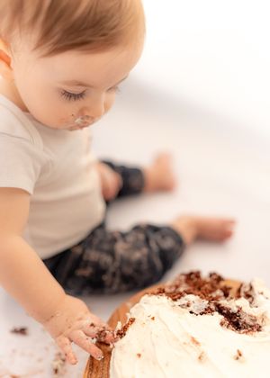 A baby smashing a white frosted cake with chocolate shavings during a first birthday cake smash photo session.