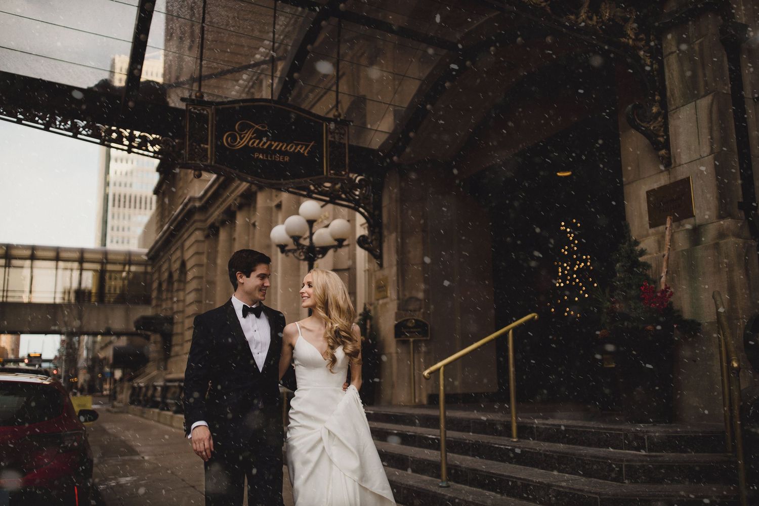 Bride and groom share a romantic moment in falling snow outside the Fairmont Palliser in downtown Calgary, by a Calgary wedding photographer