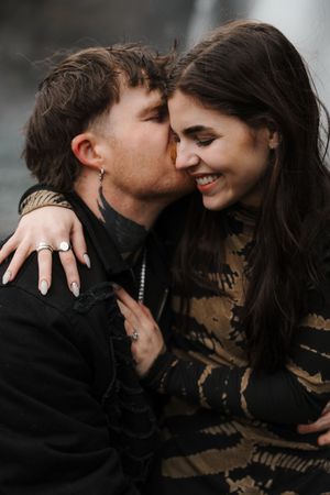 A couple shares a tender moment as a man kisses a smiling woman on the cheek outdoors.