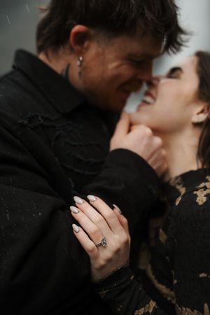 Couple in black lace outfits share an intimate moment, woman showing engagement ring with elegant manicure.