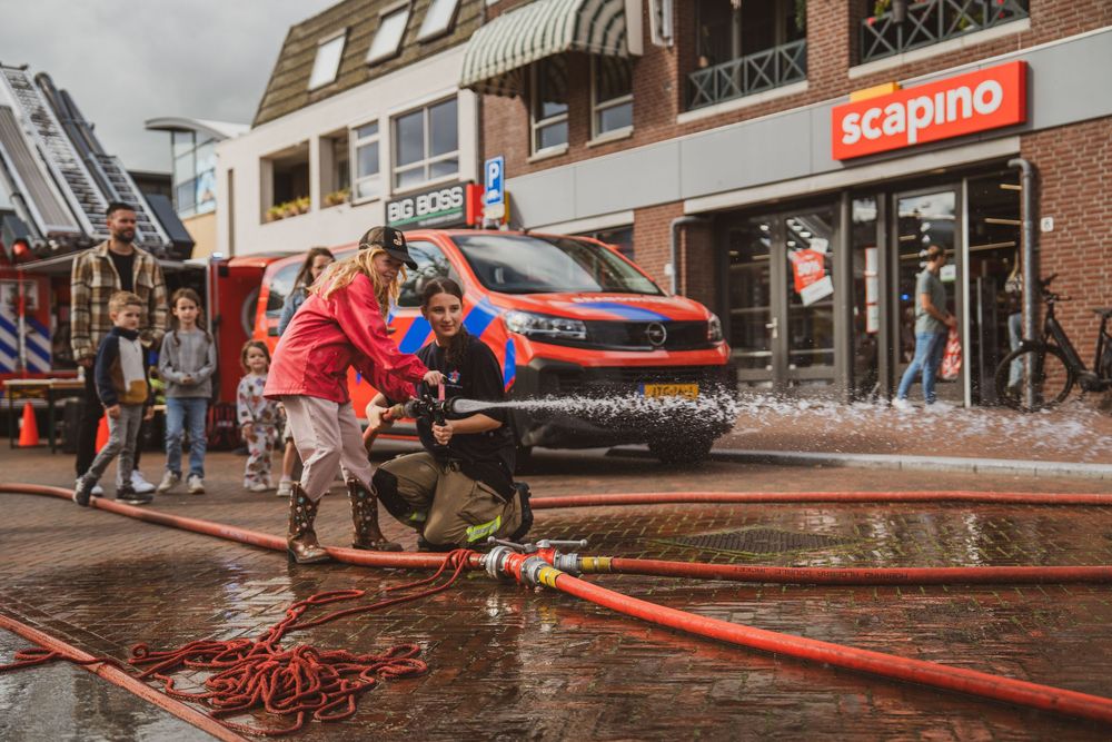 Firefighters manage a hose on a wet street near a Scapino store during an emergency response exercise.
