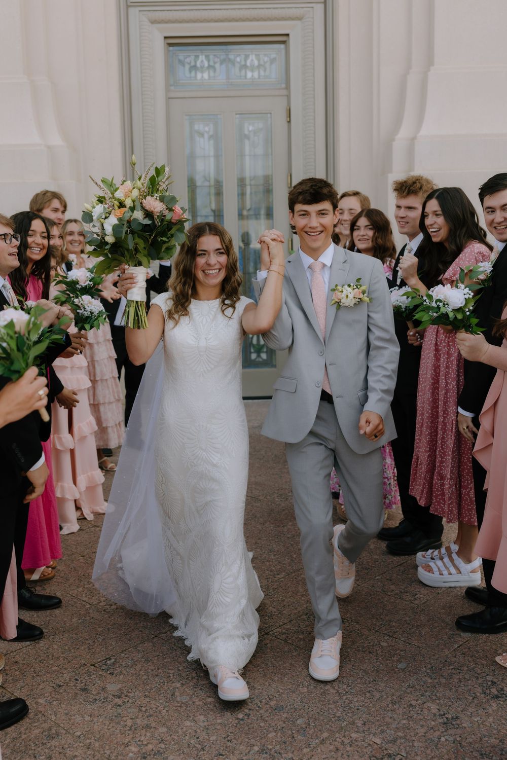 Bride and groom exiting temple wedding ceremony through cheering guests in pink attire.