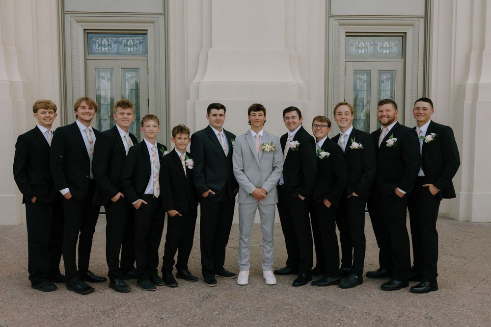 Groom in light gray suit stands with groomsmen in black suits and ties for wedding portrait.