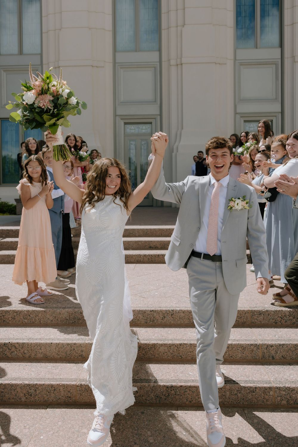 Excited bride and groom raise joined hands triumphantly on temple steps as guests celebrate their wedding exit.