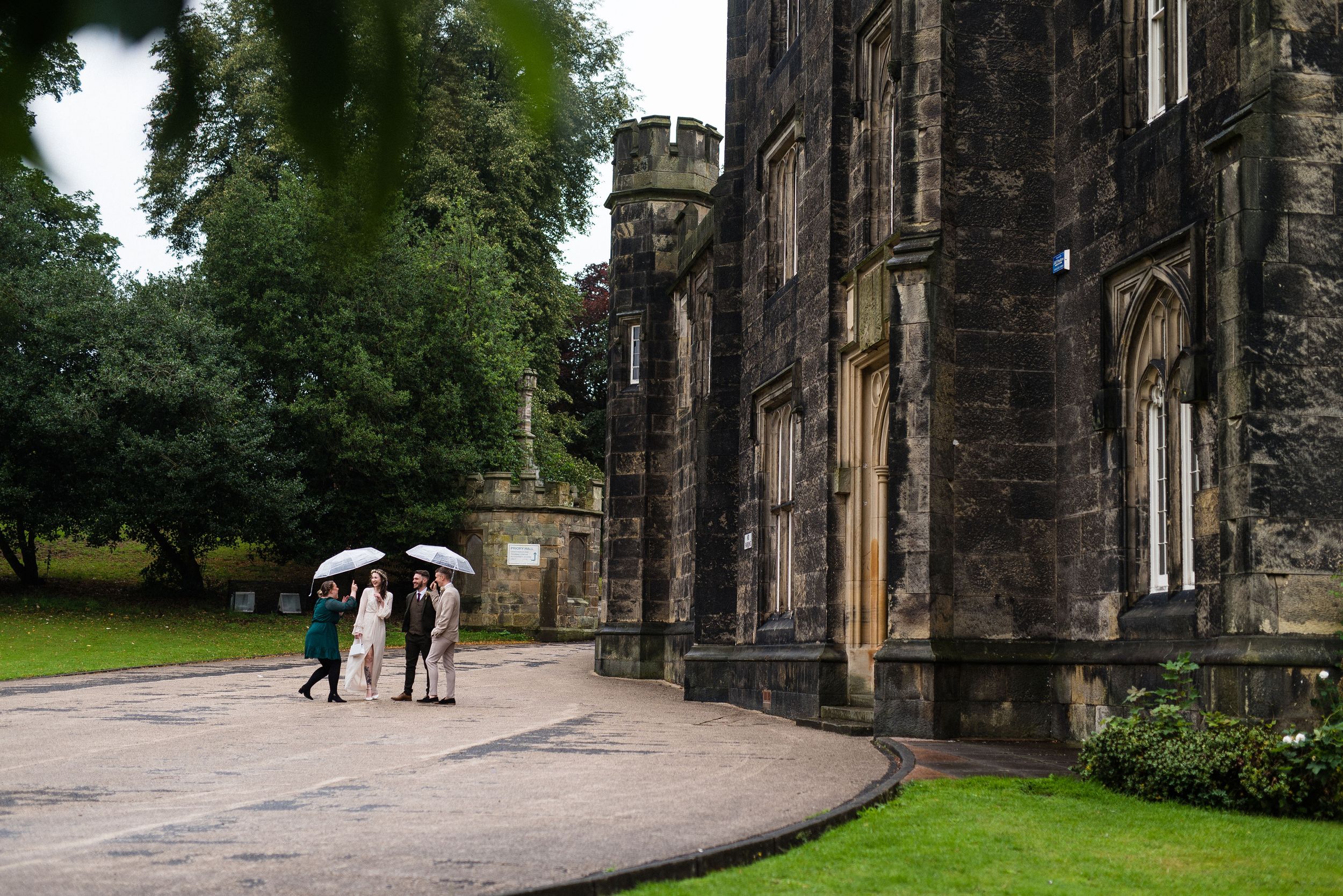 Georgia and Adam with guests and umbrellas outside their wedding ceremony on a rainy day