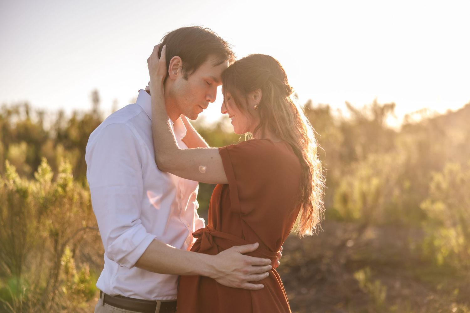 Couple embracing while standing on a coastal cliff overlooking the ocean surrounded by golden wildflowers.