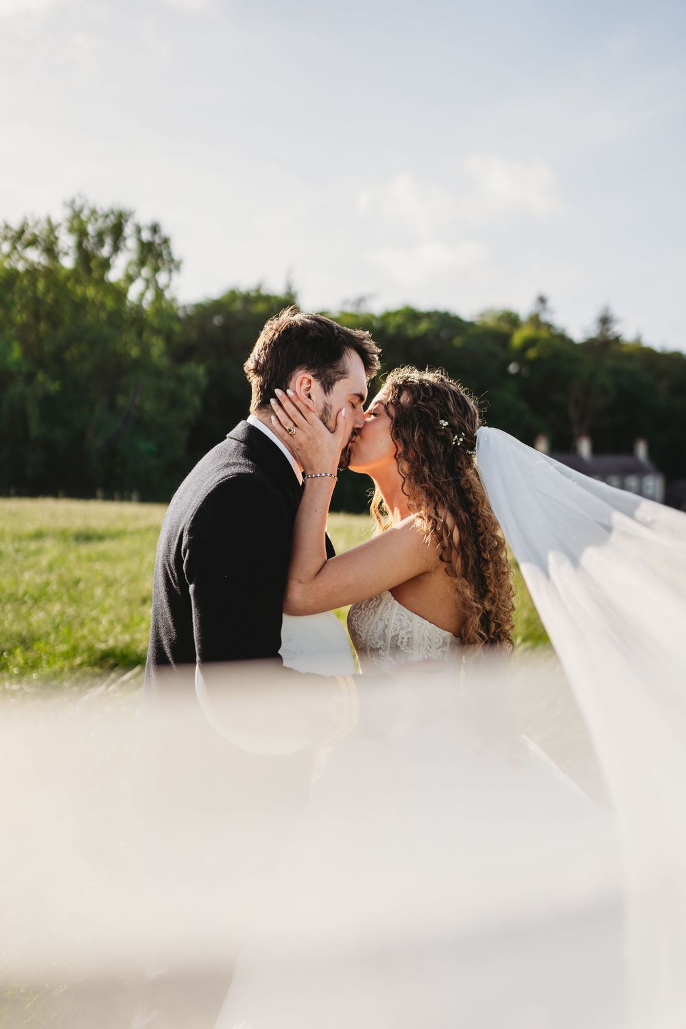 A bride and groom share a romantic kiss outdoors on their wedding day, with the veil flowing in the foreground. Tan y Graig Aberystwyth