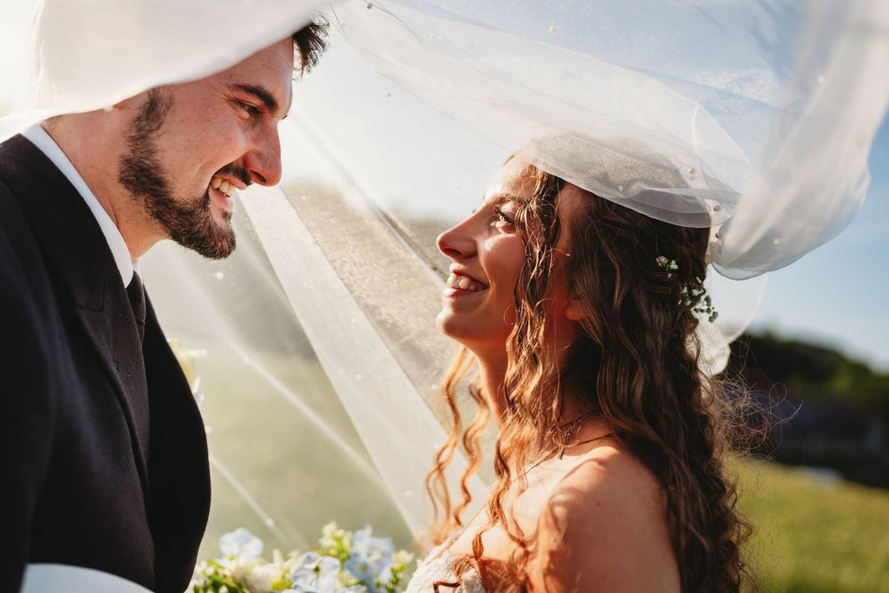 A joyful bride and groom share a romantic moment under a flowing white veil on their wedding day.
