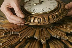 Gros plan sur les mains d’un artisan travaillant à la restauration d’une horloge ancienne et de ses ornements dorés.