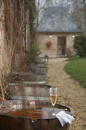 Terrasse et jardin d’une maison de campagne, avec une coupe de champagne posée sur une table.
