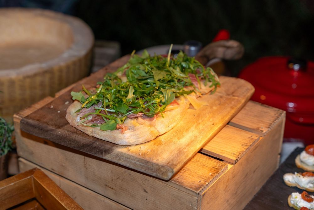 Rustic flatbread pizza topped with fresh arugula and prosciutto served on a wooden cutting board.