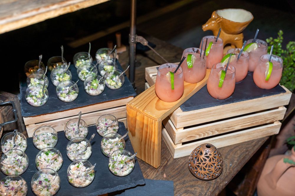 Elegant cocktail display with pink drinks garnished with lime and herb-filled glasses arranged on wooden crates.