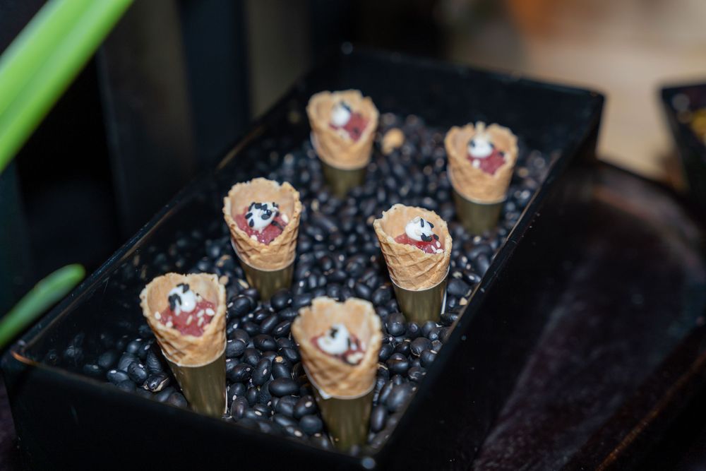 Mini waffle cones filled with cream and berries displayed upright in coffee beans on a dark tray.