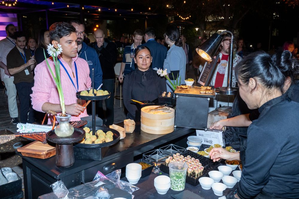 Guests enjoy a buffet spread at an elegant evening event, with servers presenting dishes at a well-lit food station.