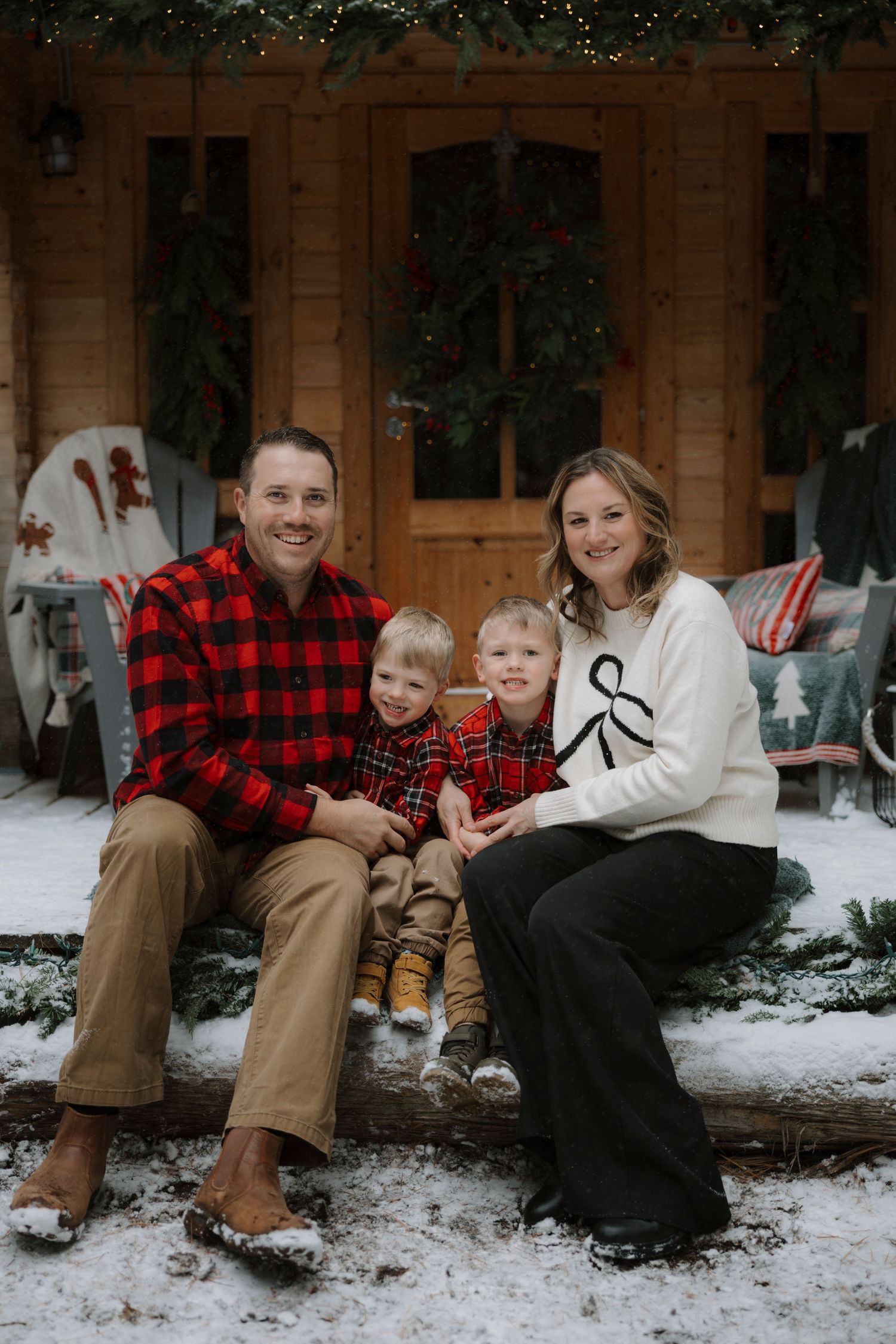Family posing in front of a festive Christmas-decorated wooden cabin in a pine forest.
