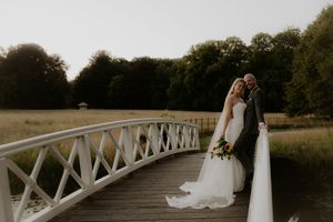 Bride and groom posing on a white ornamental bridge surrounded by lush greenery at golden hour.