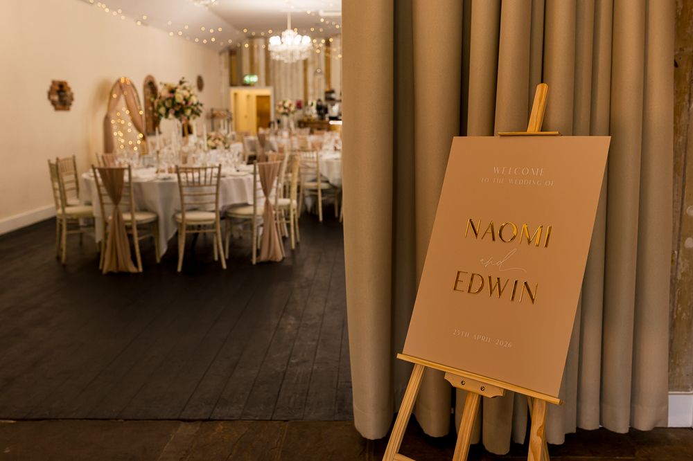 Elegant wedding reception venue with round tables and a welcome sign reading Naomi and Edwin on a wooden easel.