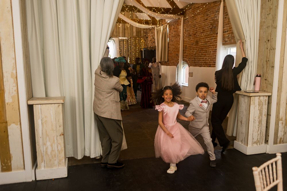 Two children in formal attire dance joyfully at a wedding reception in a rustic barn venue.