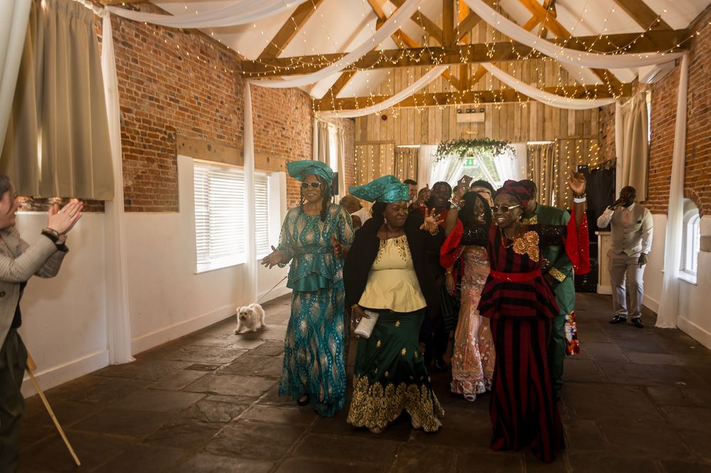 Guests in colorful traditional attire dancing and celebrating inside a rustic brick wedding venue decorated with fairy lights.
