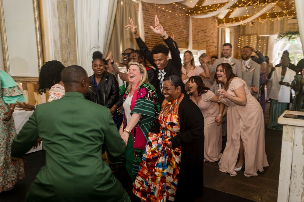 Joyful wedding guests dancing and celebrating together in a decorated reception hall with string lights.