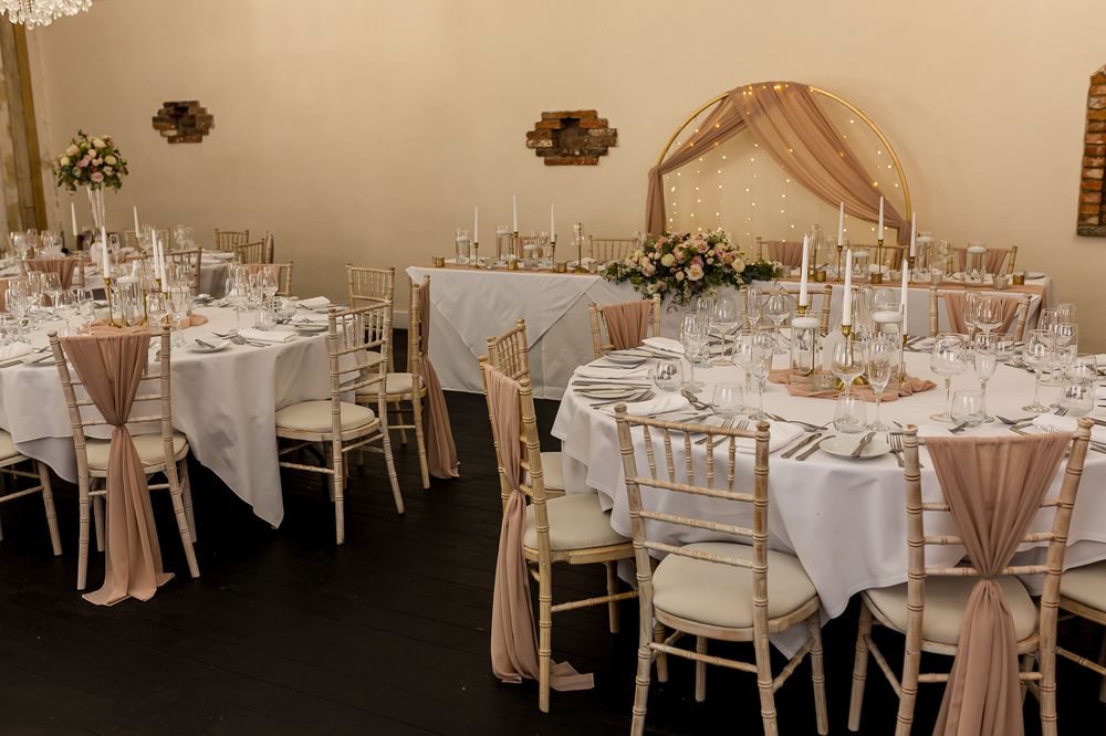 Elegant wedding reception room with round tables, white linens, blush chair sashes, candles, and floral centerpieces.