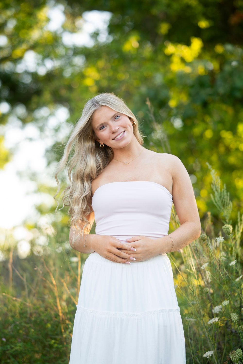 Smiling blonde woman in white tube top and skirt posing outdoors in golden light.