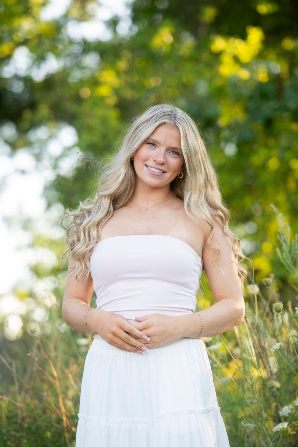 Young blonde woman in pink tube top and white skirt smiling in a sunny green meadow.